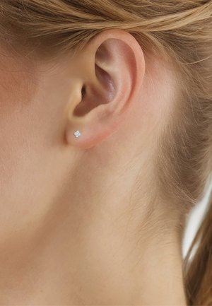 Primo piano dell'orecchio di una persona con capelli biondi corti che indossa un piccolo orecchino a bottone tondo con diamante bianco sul lobo dell'orecchio.