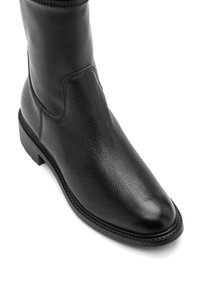 Musta nahkaiset nilkkabot, joissa on sileä pinta, pyöreä kärki ja hieman teksturoitu päälline. Varustettu matalalla korolla ja minimikokoisilla ompeilla.