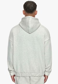Un hoodie surdimensionné gris clair avec une capuche à cordon, des poignets et une taille côtelés. Fabriqué à partir d'un tissu doux et texturé avec une coupe décontractée.
