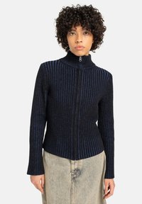 Zwarte en blauwe ribgebreide trui met een hoge kraag en ritsluiting, met lange mouwen en een aansluitende pasvorm.