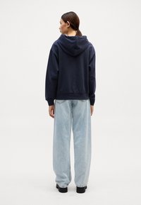 Sweatshirt azul-marinho com capuz, de corte descontraído e mangas longas, combinado com jeans de perna larga azul-claro e sapatos de plataforma pretos.