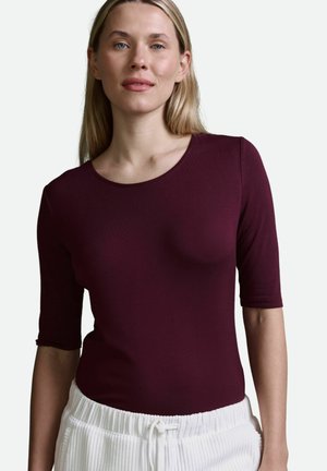 Burgunderfarbenes, figurbetontes Oberteil mit glatter Textur und halben Ärmeln, kombiniert mit weißen, gerippten Jogginghosen mit Kordelzug. Schlichtes, rundes Halsdesign.