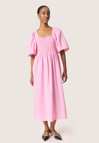 Rosa randig midiklänning med smockad midja och puffärmar, med fyrkantig halsringning och lätt tyg. Skor: svarta spetsiga ballerinas.