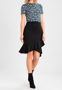 Modrý a bílý top s květinovým vzorem a krátkým rukávem, doplněný černou asymetrickou sukni s volány. Texturovaná tkanina s vypasovaným pasem.