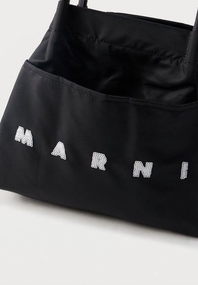 Μαύρη υφασμάτινη τσάντα tote με λευκά παγιετέ γράμματα που σχηματίζουν τη λέξη "MARNI" στο εμπρόσθιο μέρος, με δύο λουριά ώμου.
