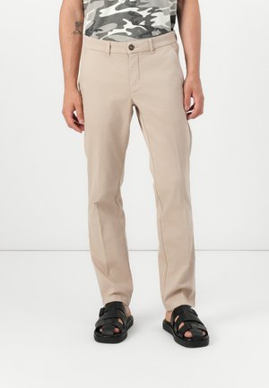 Beige chinos med almindelig pasform, knaplukning og sidelommer, parret med sorte strop sandaler. Glat stofstruktur.
