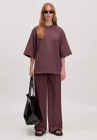 Oversized mauve T-shirt, wijde bijpassende broek, zwarte glanzende handtas, zwarte zonnebril, gladde textuur, relaxte pasvorm, minimalistische accenten.