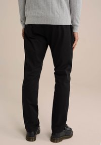 Pantaloni negri din bumbac cu croială slim, asortați cu un pulover gri. Se observă tivul texturat al puloverului, materialul neted și pantofii negri rezistenți.