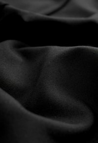 Material textil negru cu o textură netedă, prezentând pliuri delicate și reflecții subtile de lumină, evidențiind aspectul său moale și opac.