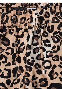 Close-up of beige fabric with black and brown leopard print, featuring an elastic waistband and black drawstrings with metal tips.