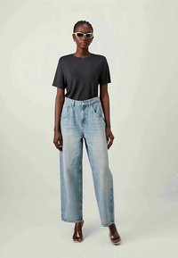 Sötétszürke póló, laza fitneszű, világoskék farmernadrág széles lábakkal, magas derekú, elülső zsebekkel és minimális varrással. Bézs szandál és napszemüveg.