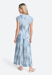 Blusa blu a righe con maniche a campana abbinata a pantaloni larghi. Il tessuto appare leggero e liscio. Accentuato da una morbida caduta.