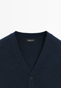 Navyblåstickad cardigan med ribbad textur, V-ringning och knappstängning. Märkesetikett synlig i halsringningen.