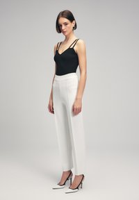 Zwart geribbelde top met dunne bandjes, gecombineerd met hoge witte wijde broek en zwart-witte puntige hakken.