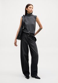 Siva brezrokavna majica z naramnicami in dvignjenim ovratnikom, v kombinaciji z visokim pasom širokimi črnimi jeans hlačami. Model nosi črno torbo. Gladke teksture, minimalističen dizajn.