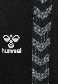 Schwarze Sportbekleidung mit einem weißen "hummel"-Logo und einem kontrastierenden grauen Zickzackmuster an der Seite. Glatte Stoffoberfläche.