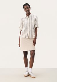 Stribet linned skjorte med knap i cremefarvet med mørke striber, parret med en beige bomuldsnederdel. Hvide sokker og grå sneakers fuldender outfittet.