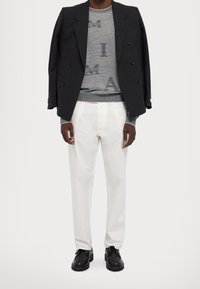 Svart dubbelknäppt kavaj, grå tröja med bokstäver, vita byxor och svarta snörskor. Släta tyger, strukturerad design.