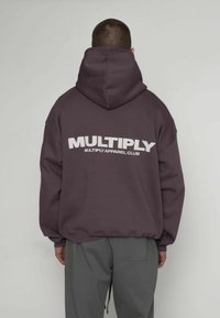 Bluza z kapturem w ciemnym odcieniu fioletu, z dużym, białym logo "MULTIPLY" na plecach. Wykonana z miękkiego materiału, luźnego kroju, z regulowanym sznurkiem.