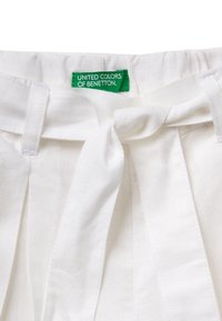 Cinturilla de lino blanco con un detalle de lazo, que cuenta con una etiqueta verde que dice "UNITED COLORS OF BENETTON" en texto blanco.