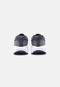 Ζευγάρι αθλητικά παπούτσια σκούρου γκρι χρώματος με λευκές σόλες, εμφανίζονται από πίσω σε απλό φωτεινό φόντο.