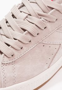 Szary zamszowy sneaker o fakturowanej powierzchni, płaskie plecione sznurowadła, biała gumowa podeszwa i dyskretne perforacje po boku.