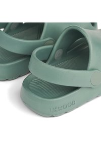 Zöld gumiszandálok, két állítható pánttal, textúrált talppal és kiemelkedő logóval a talpán. Sleek és minimalista dizájn.