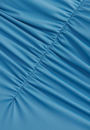 Svetloblue tkanina z teksturirano površino, ki ima nabrane dele, ki ustvarjajo valove in globino po materialu.