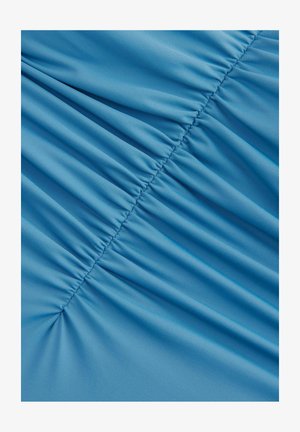 Lyseblåt stof med struktureret overflade, der har sammensamlede sektioner, som skaber bølger og dybde i materialet.