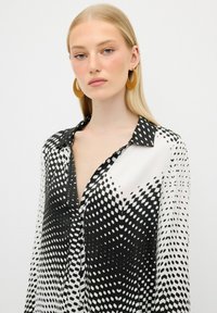 Blusa bianca e nera con motivo a pois, tessuto leggero, maniche lunghe e colletto, con una parte anteriore a bottoni parziale.