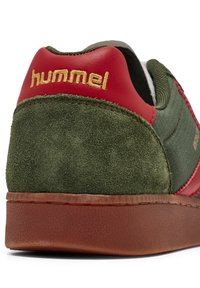 Zöld velúr sneaker piros bőr díszítéssel, arany "hummel" márkanevével és bordázott barna gumitalppal.