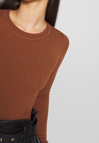 Top marrón de manga larga acanalado con cuello redondo, combinado con un cinturón negro de textura suave y detalles en hardware dorado.