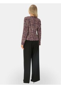 Dopasowana fioletowa tweedowa marynarka z teksturowanej tkaniny i dopasowanym krojem, zestawiona z czarnymi spodniami o szerokich nogawkach i wysokim stanem.
