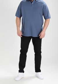 Blå pikétröja med krage, med en liten logotyp. Kombinerad med svarta jeans och vita sneakers. Slätt tyg, avslappnad passform.