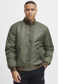 Olive green bomber jacket made of shiny, quilted material. Features a zip front, two side pockets, and ribbed cuffs with a collar.