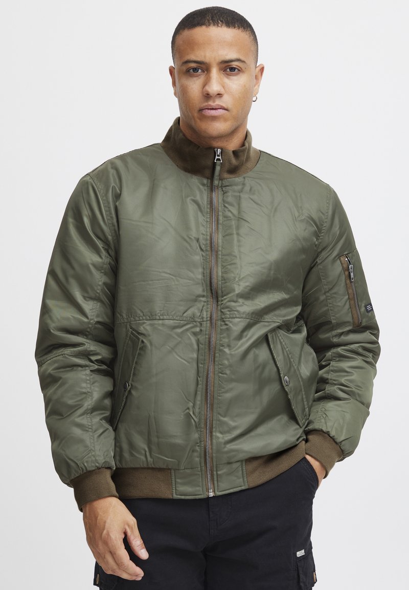 Olive green bomber jacket made of shiny, quilted material. Features a zip front, two side pockets, and ribbed cuffs with a collar.