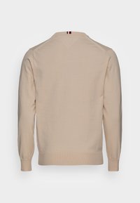Maglione in cotone beige con maniche lunghe, scollatura rotonda e polsini e orlo a coste. Sul retro presenta un dettaglio a strisce vicino al collo.