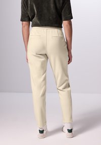 Beige op maat gemaakte broek met een slim fit, twee achterzakken en een soepele textuur. Gecombineerd met lichte sneakers met een groene accent.