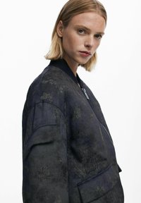 Navy bomber jacket with floral embroidery, ribbed collar, and zip closure. Features a textured fabric and side pockets.