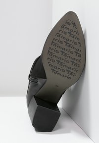 Botín negro de tacón con un exterior texturizado y tacón cuadrado; presenta una cremallera lateral y el nombre de la marca impreso en la suela. Talla 36.