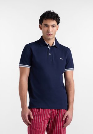 Polo bleu marine avec une patte de boutonnage à deux boutons, logo blanc et accents rayés sur le col et les manches. Confectionné dans un tissu lisse.