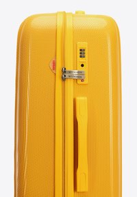 Gele hard-shell koffer met een textuur van gaaspatroon, uitgerust met een combinatie-slot, dubbele ritsen en een zijhandgreep.