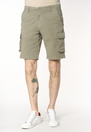 Pantaloncini cargo khaki da uomo con tasche laterali, indossati con scarpe da ginnastica bianche, che mostrano un tatuaggio di piuma sulla parte inferiore della gamba sinistra.
