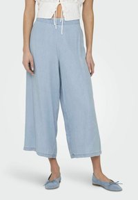 Pantalones anchos de color azul claro, hechos de una tela suave, con una cinturilla elástica y un corte holgado, combinados con zapatos planos de color azul a juego.