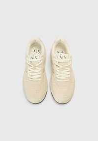 Beežid seemisnahast tossud, millel on pooridega detailid, valged paelad ja musta kummist tald. Sisetaldel on logo. Vaade ülalt.