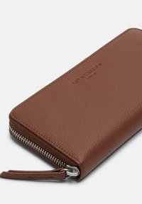 Brown leather wallet with a textured finish, featuring a silver zipper and a wrist strap. Subtle embossed branding on the surface.