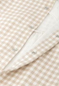 Tejido de cuadros beige y blanco con broches plateados visibles, que presenta una suave capa interior. La costura es limpia y está terminada.