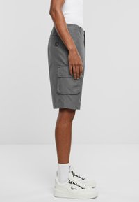 Shorts cargo gris avec poches latérales, devant plat et coupe décontractée. Matériau en coton, longueur au genou, associés à des baskets blanches et des chaussettes montantes.