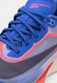 Chaussure de course Nike Zoom Fly bleue avec lacets bleus, accents roses et tige en mesh respirant visible en gros plan.