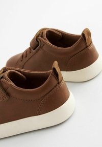 Brązowe skórzane sneakersy o teksturowanym wykończeniu, z białymi gumowymi podeszwami i tkaninowymi akcentami na pięcie. Sznurowana konstrukcja z przeszyciami.